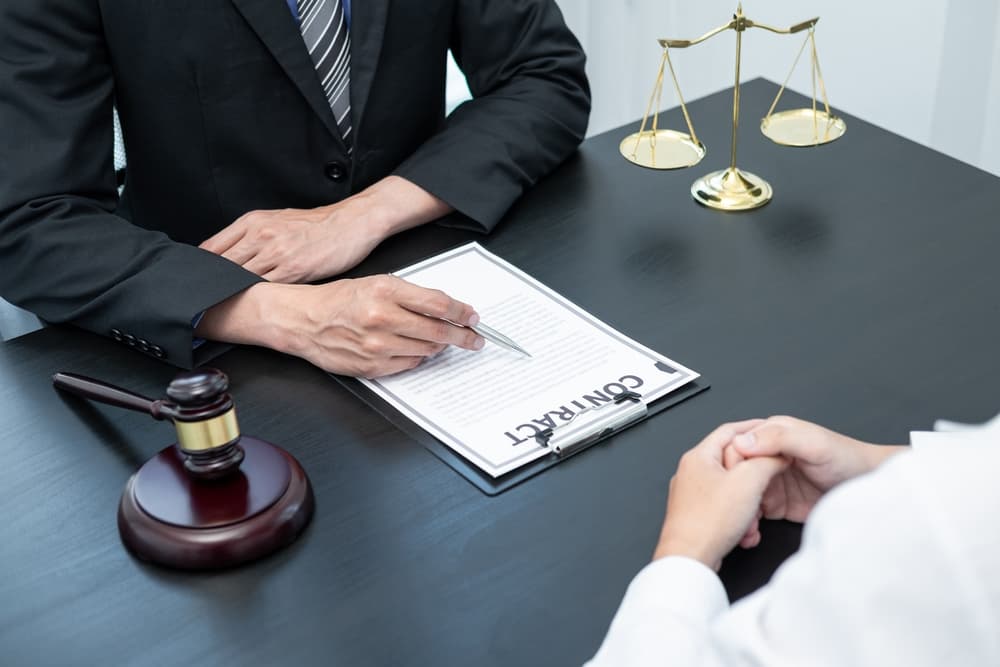 A male lawyer or counselor discussing a negotiation in a legal case with a client, meeting with a document contract in an office. Law and justice, attorney, lawsuit concept.