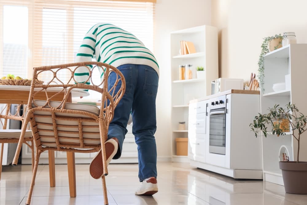 A man tripping over a chair in the kitchen.
