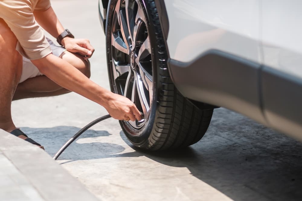 man driver hand inflating tires of vehicle, removing tire valve nitrogen cap for checking air pressure and filling air on car wheel at gas station.