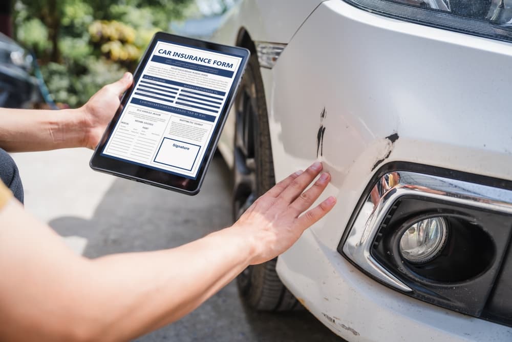 A man completes a car insurance form following a car accident. His comprehensive motor insurance covers the damage, and he submits a claim report while discussing it with an adjuster.