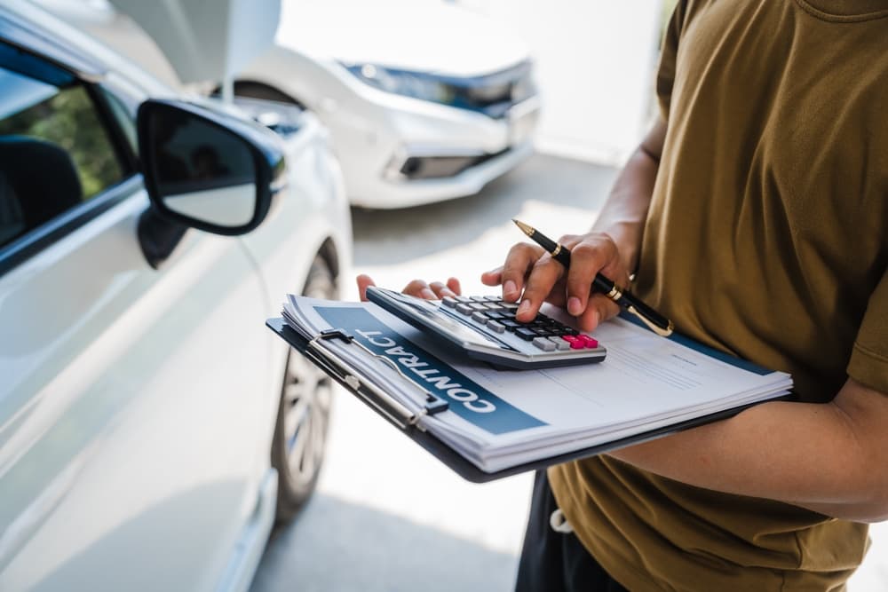 A man completes a car insurance form following an accident. Comprehensive motor insurance covers vehicle damage. He files a claim and speaks with an adjuster.