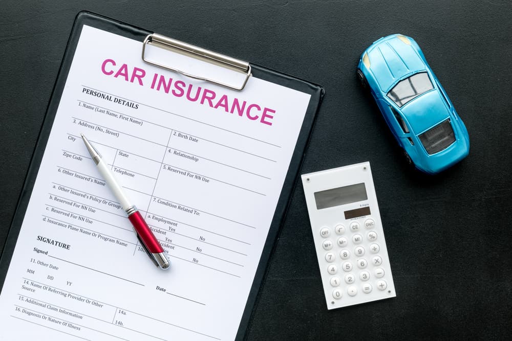 Car insurance concept featuring a form, a toy car, and a calculator arranged on a black background, viewed from above.