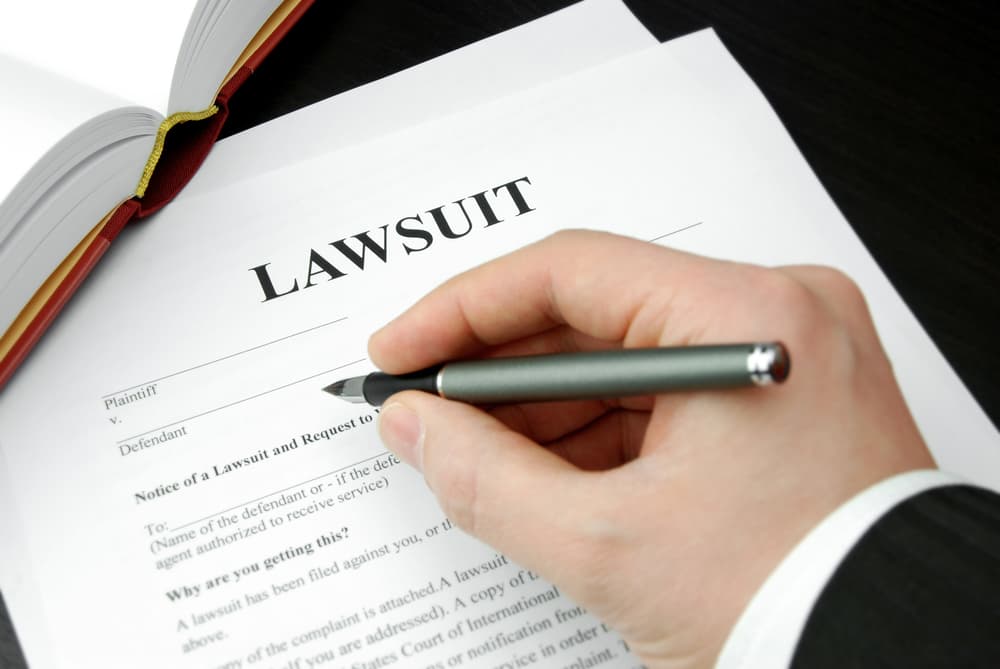 A lawsuit form held by an attorney's hand with a pen.