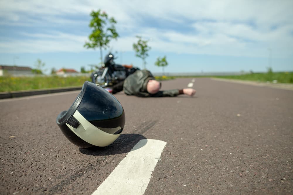 A biker helmet lying on the street next to a crashed motorcycle, representing the aftermath of a serious accident. 