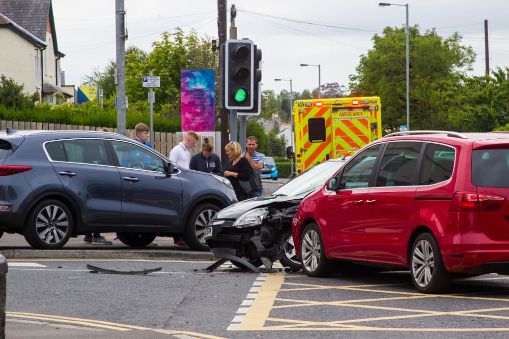 A multi-car collision at an intersection with bystanders, an ambulance, and traffic lights.