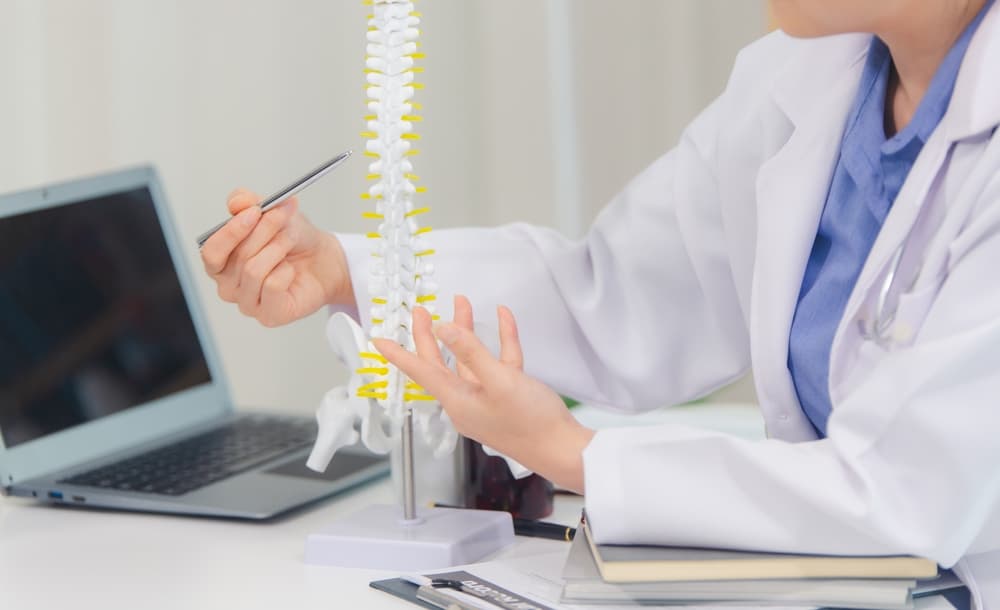 An orthopedic doctor explains a spinal model to a patient, discussing back pain and spine disorders.