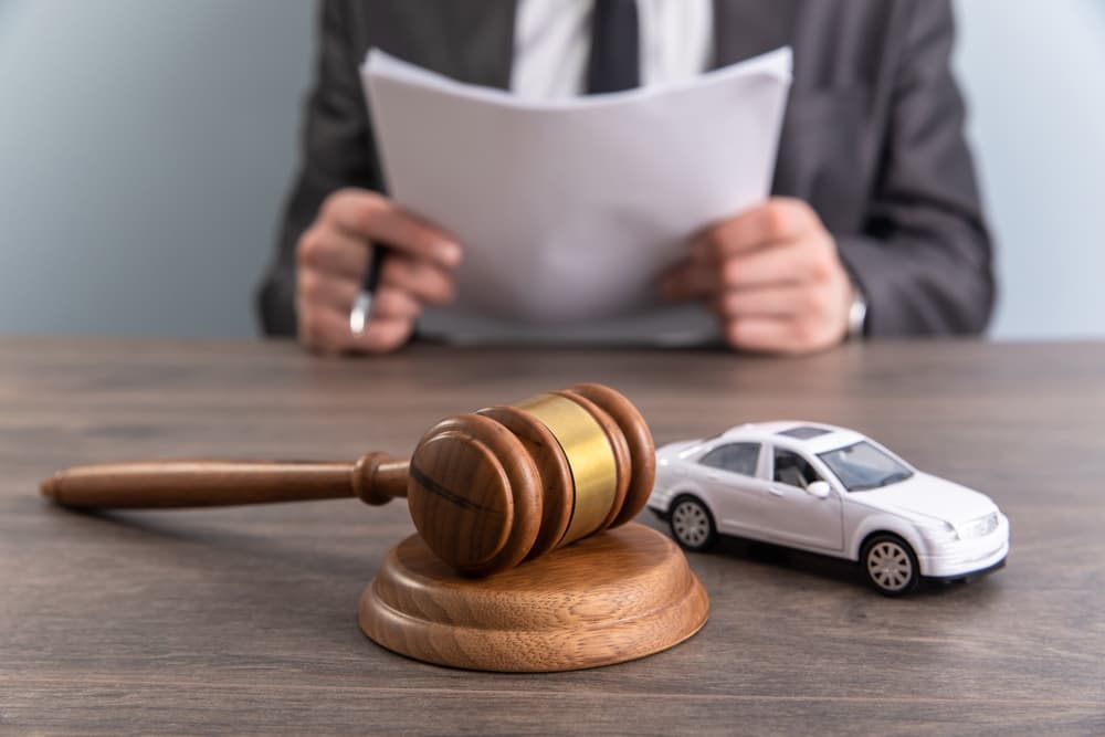 A lawyer reviews documents beside a gavel and car model, symbolizing legal protection and future security.