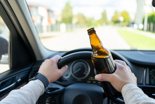 Driver holding a beer bottle while steering a car, showing drunk driving.