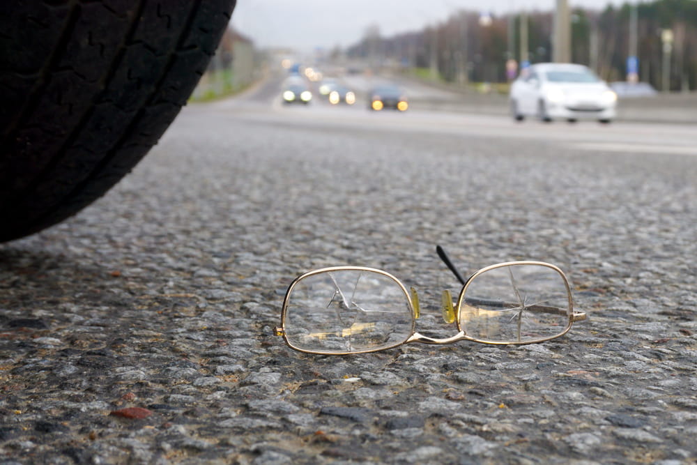 Broken eyeglasses on roadway near vehicle tire illustrating serious pedestrian accident aftermath